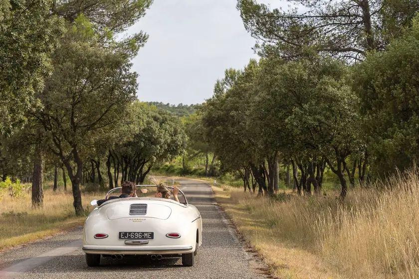 Voiture ancienne blanche décapotable sur un chemin bordé d'arbres