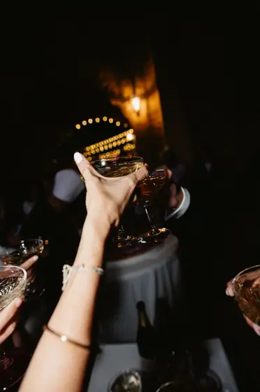 Main levant une coupe de champagne dans la nuit, bras d'invités autour