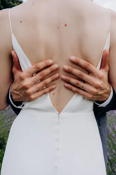 Mains du marié posées sur le dos nu de la mariée, robe boutonnée