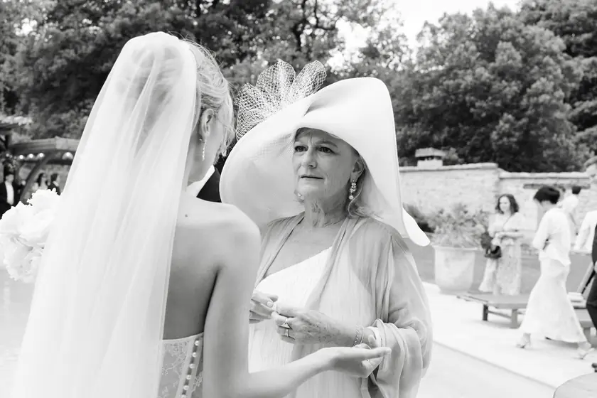 Mariée voilée de dos discutant avec une invitée en grand chapeau blanc