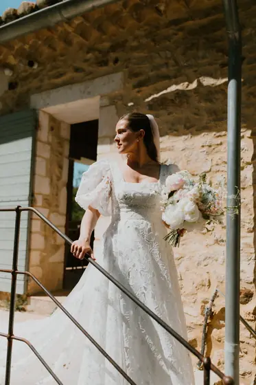 Mariée en robe à manches bouffantes sur un perron en pierre, bouquet à la main