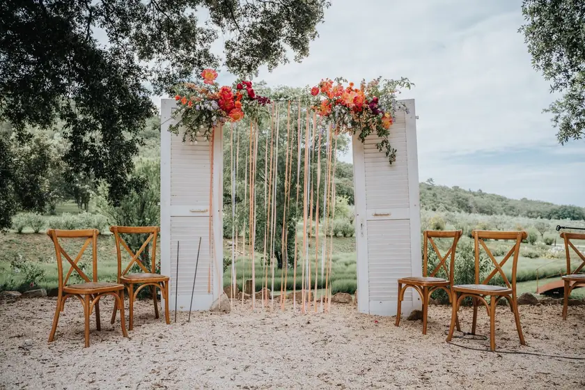 Arche de cérémonie fleurie de roses orangées entre des chaises en bois
