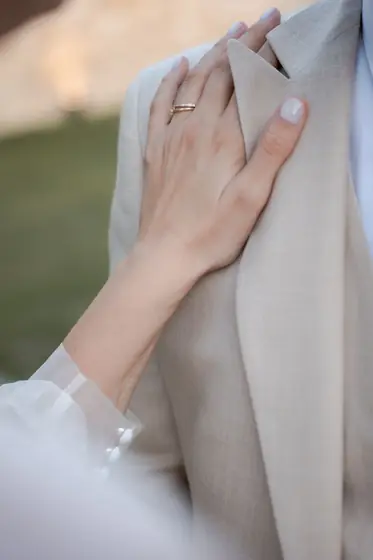 Main de la mariée portant l'alliance posée sur la veste du marié