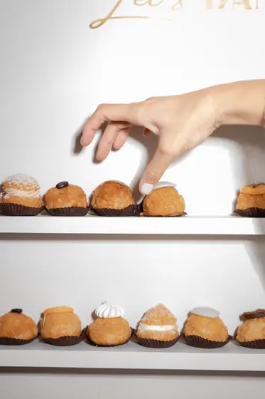 Main prenant un chou dans un présentoir de pâtisseries