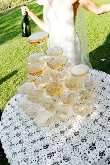 Mariée servant du champagne sur une pyramide de coupes, dans un jardin
