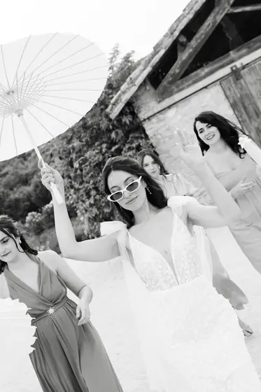 Mariée hilare avec une ombrelle, entourée de ses demoiselles d'honneur