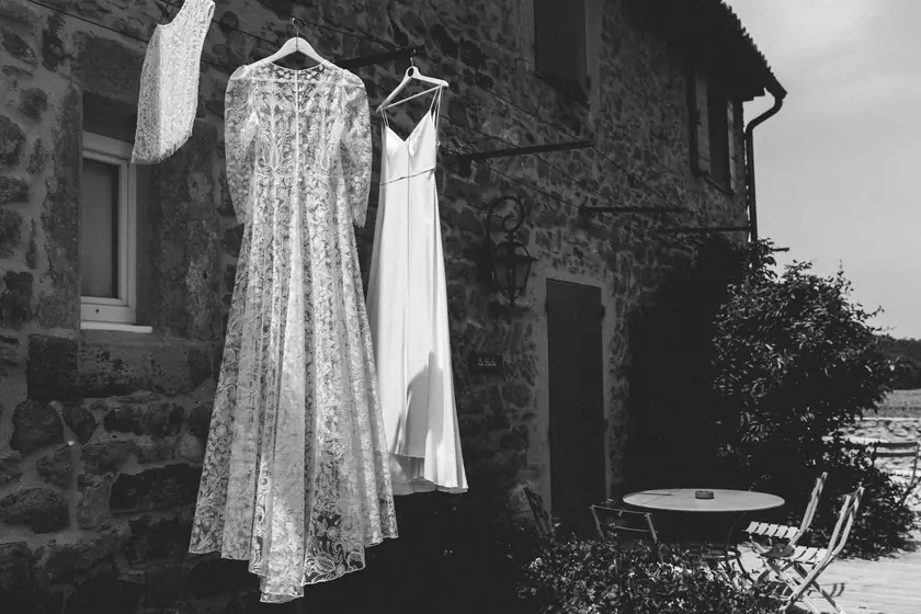 Deux robes de mariée suspendues devant une maison en pierre